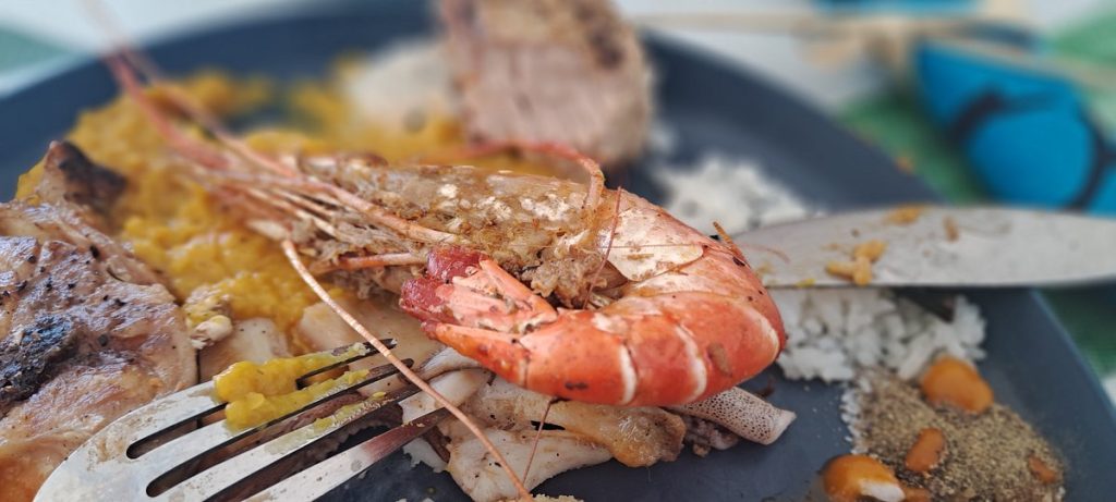 Close-up of a seafood platter with shrimp, grilled meat, and white rice on a dark plate, with a fork nearby.