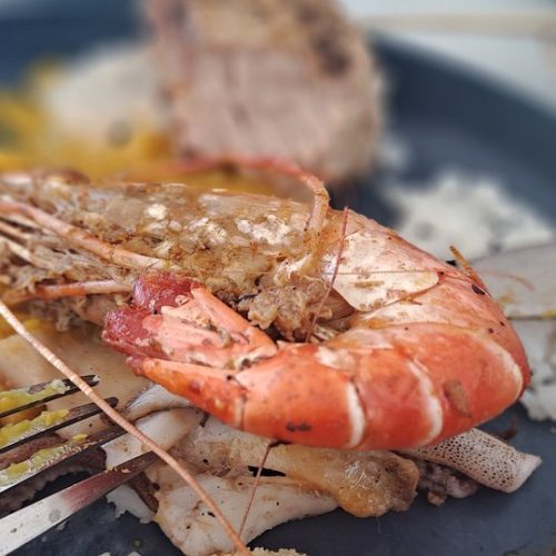 Close-up of a seafood platter with shrimp, grilled meat, and white rice on a dark plate, with a fork nearby.