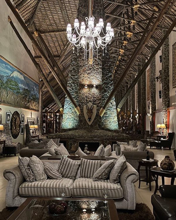Luxurious hotel lobby with a crystal chandelier, stone pillars, and multiple seating areas around a central fireplace.