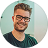 Profile photo of a smiling man with glasses and a beard, wearing a dark shirt.