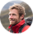 Close-up of a smiling man with light brown hair wearing a red jacket, outdoors.