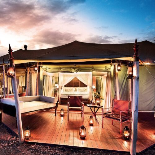 Luxurious glamping tent on a wooden deck with warm lanterns, comfortable seating, and a canopy bed inside